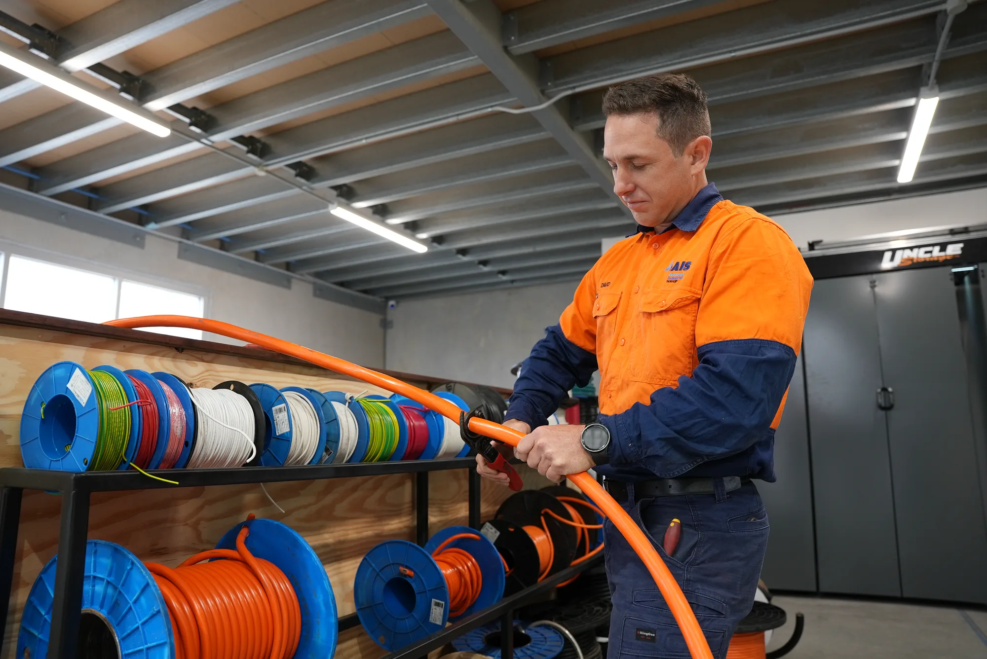 AIS team member preparing an orange electrical cable beside cable reels in a workshop